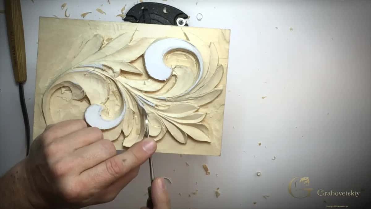 Right hand holds a thin tool low among the lobes, beside the small white curl, chips on the table