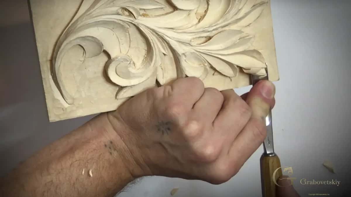 Fist round a straight gouge, its edge under a leaf near the rim of the board