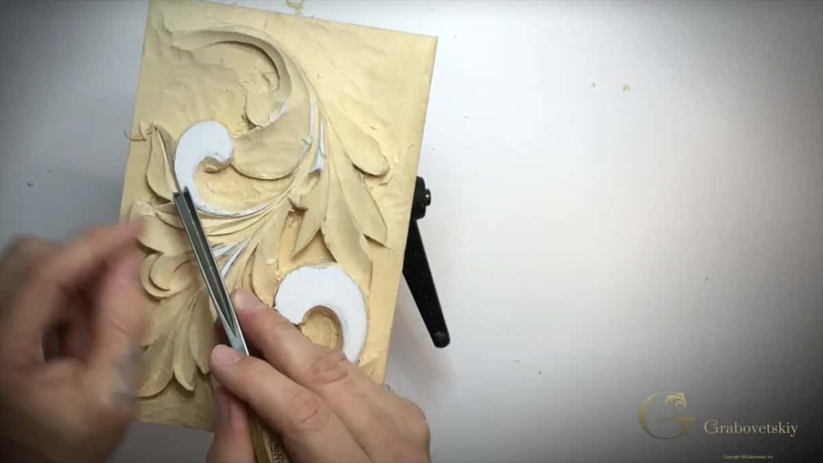 Panel stands upright in its black holder while two hands steady a straight V tool on a lobe