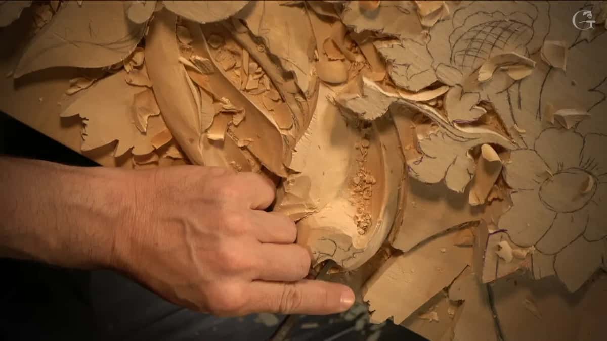 One hand holds a tool low in a deep hollow filled with loose chips