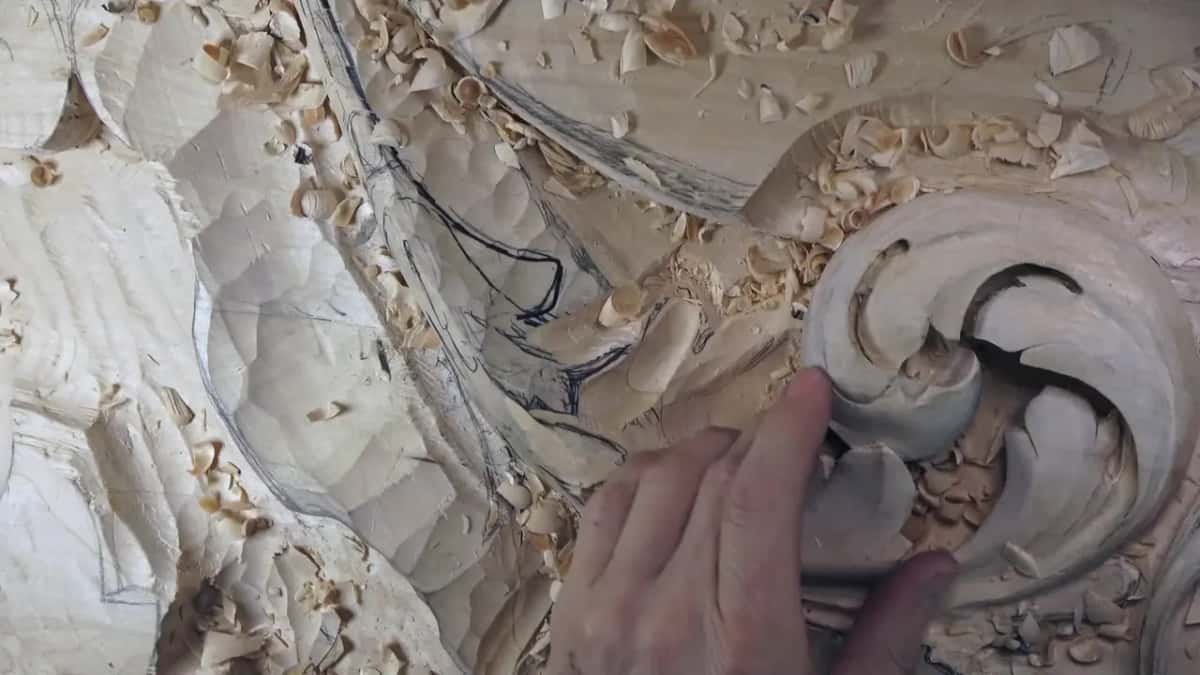 Fingertips rest on the scroll while the leaf beside it is still covered in rough facets.