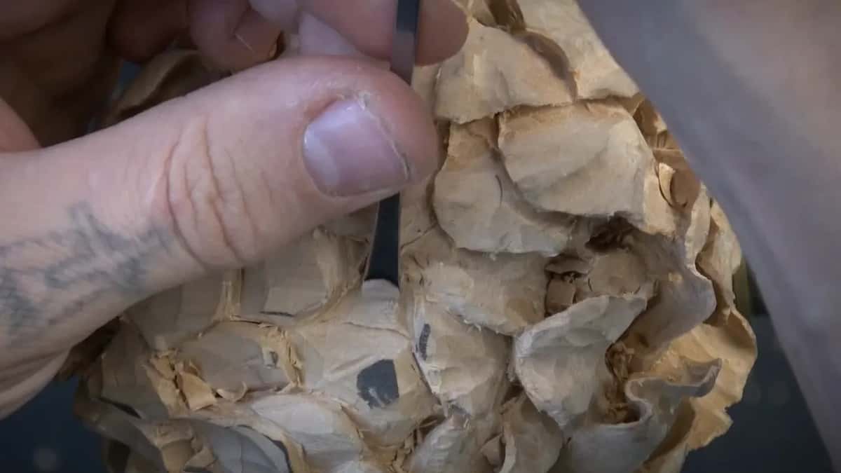 A tattooed thumb steadies a thin tool pushed down between the petals.
