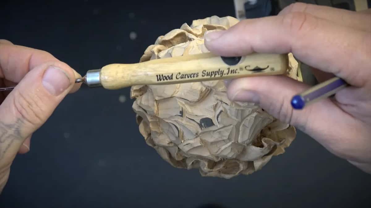 Fingers at the tip, a printed tool handle and a blue pencil gripped together over the rough flower.