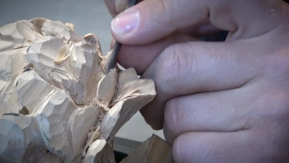 Thumb and fingers drive a fine tool down beside a curled petal