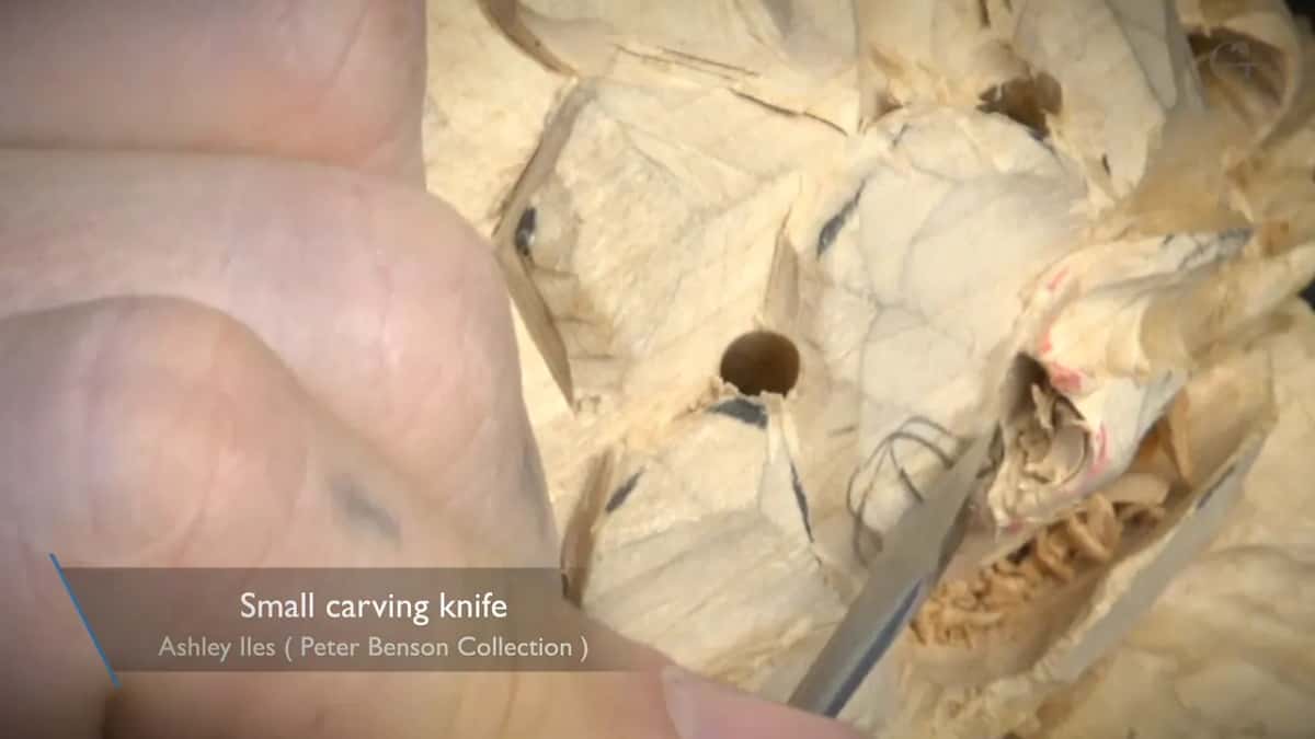 A small knife by a drilled hole, pink marks and chips around it