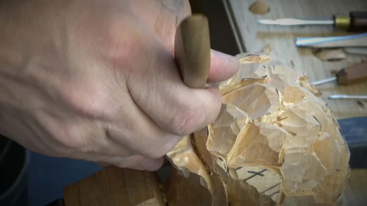 Fist around a short wood handle, more tools lying on the bench behind.