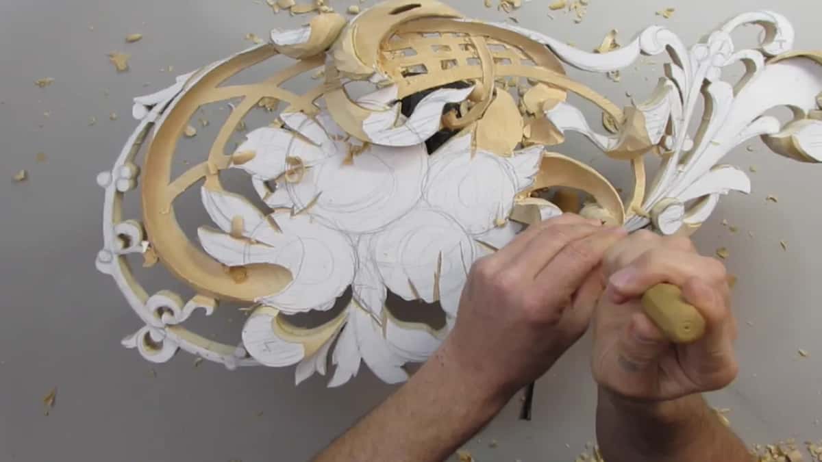 Both hands work a tool at the right side of the panel, close to the leaves