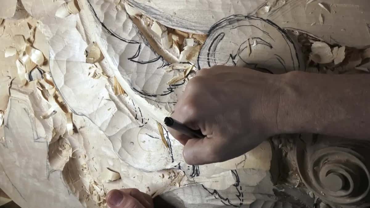 A marker redraws the scroll right onto the carved wood.