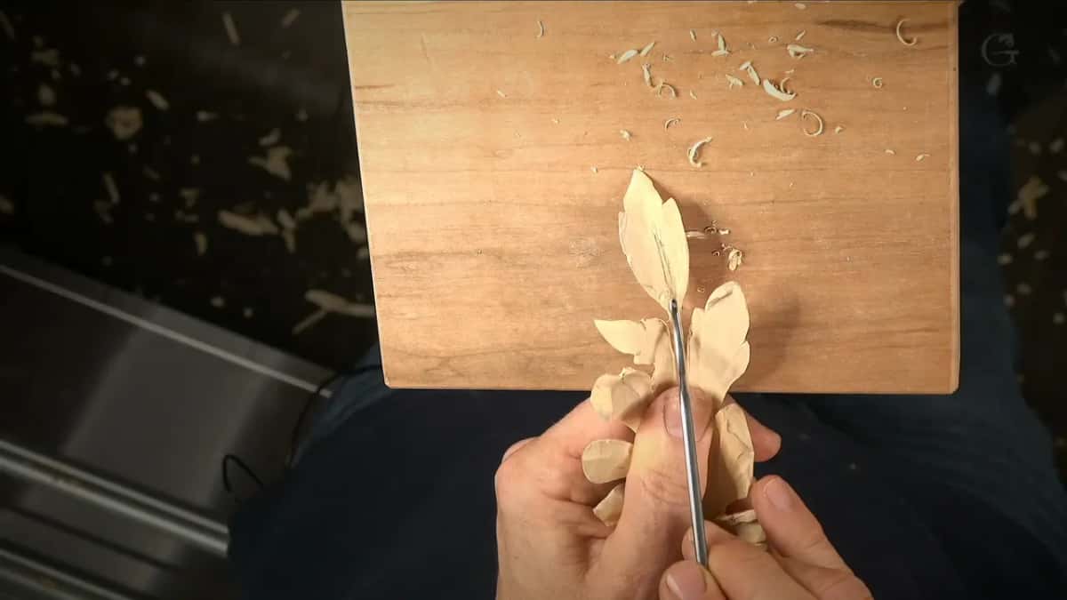 Both hands hold the leaf off the board while a slim tool runs along its spine