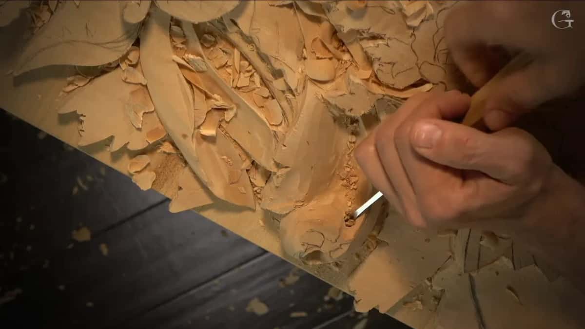 A hand works a narrow tool into the acanthus