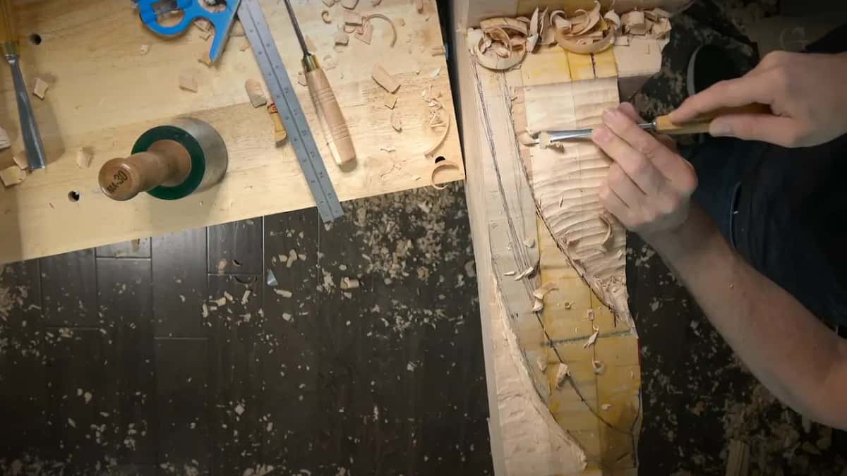 A gouge carves a channel near the top, a ruler and the blue square on the bench beside it