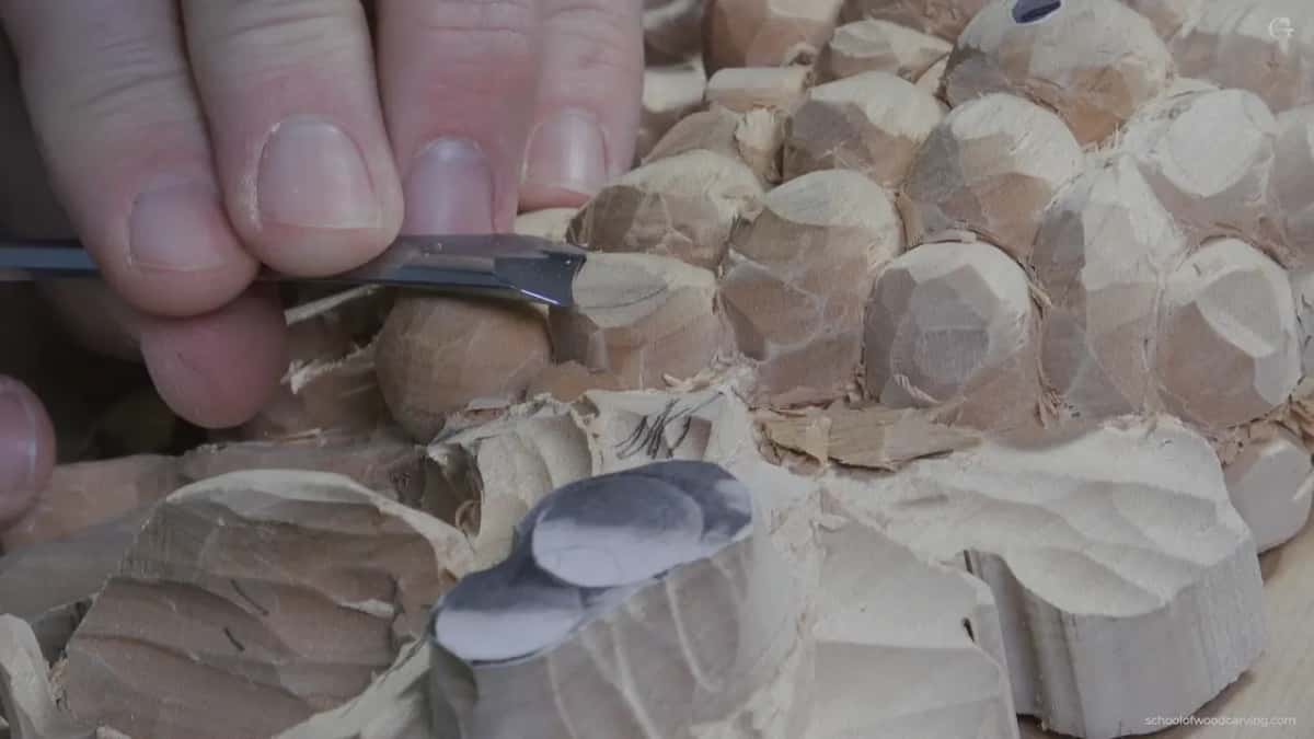 Fingers guide a flat tool over faceted grapes, a scrap of paper on the block in front