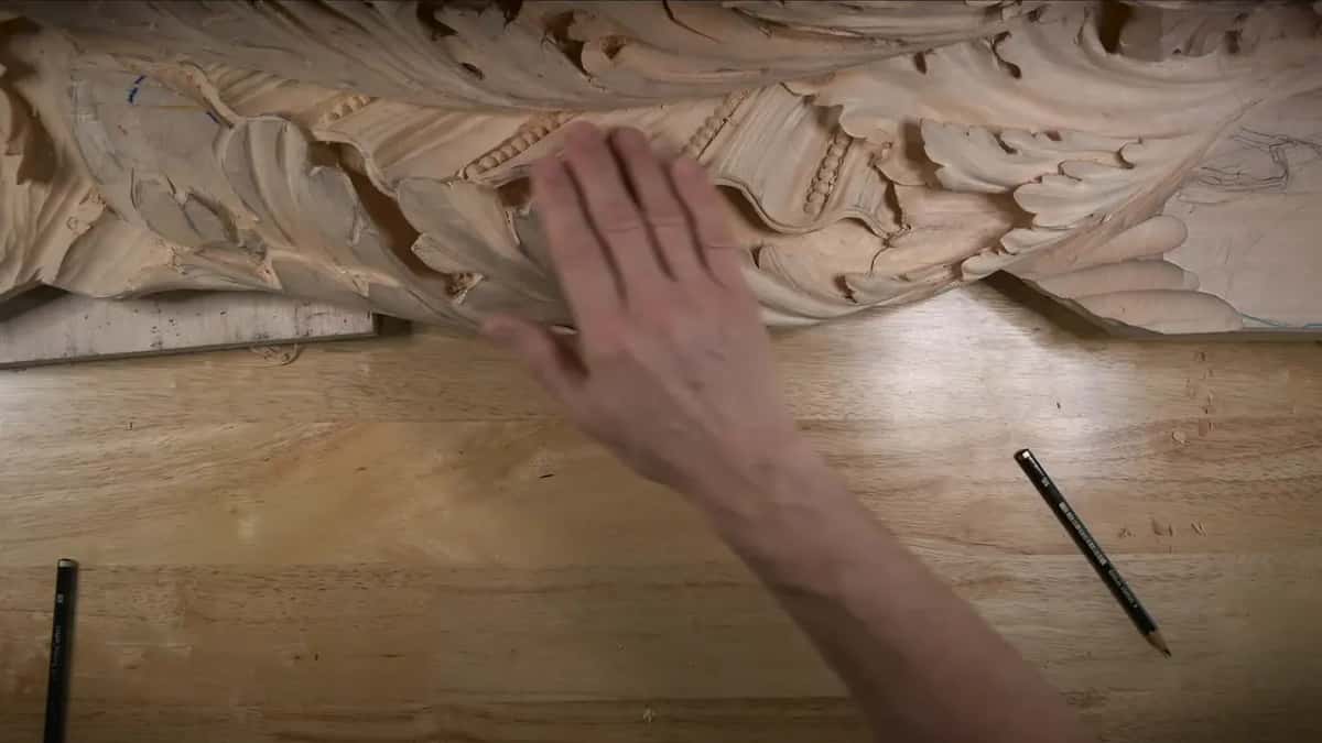 An open hand spread over the carved frieze, two pencils lying on the bench below