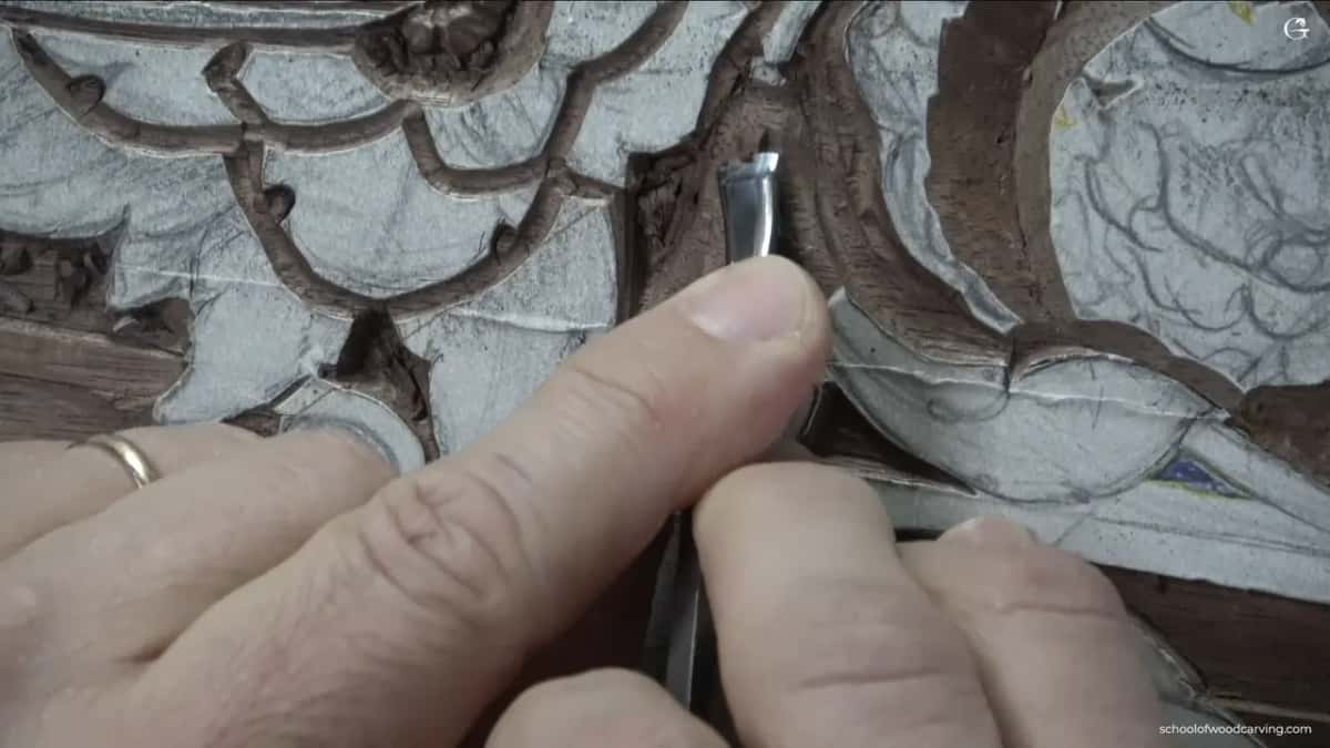 A bent tool held in the fingers at the edge of a scroll, a wedding ring on the hand behind it