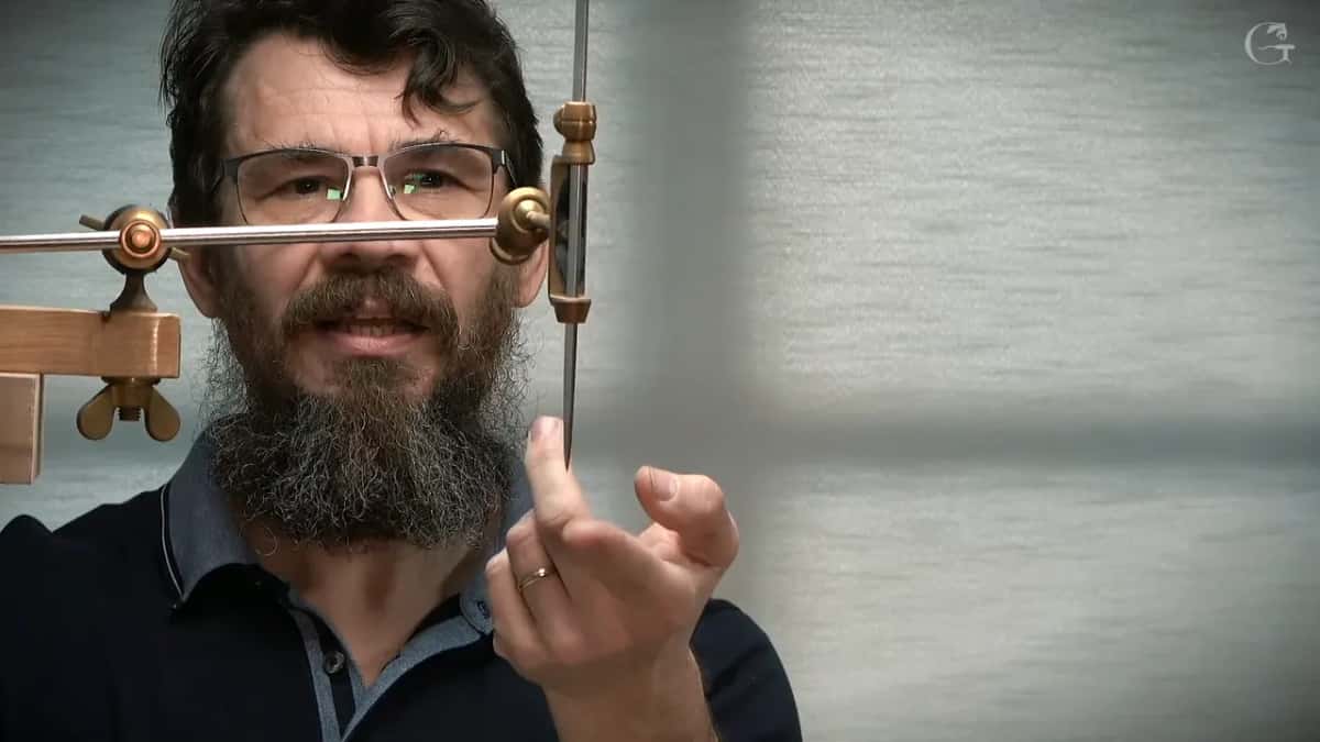 Bar and needle held up close, his face behind the brass