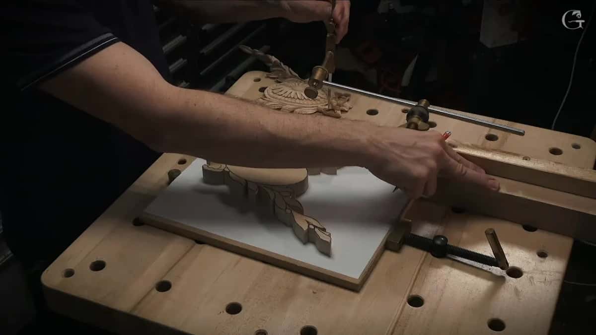 Both hands at work on the bench, one steering the arm and one holding a pencil ready