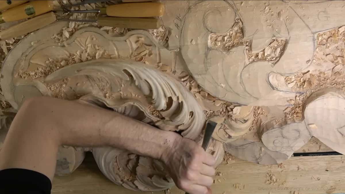 An arm reaches across the panel to set a flat chisel against the lower lobe.