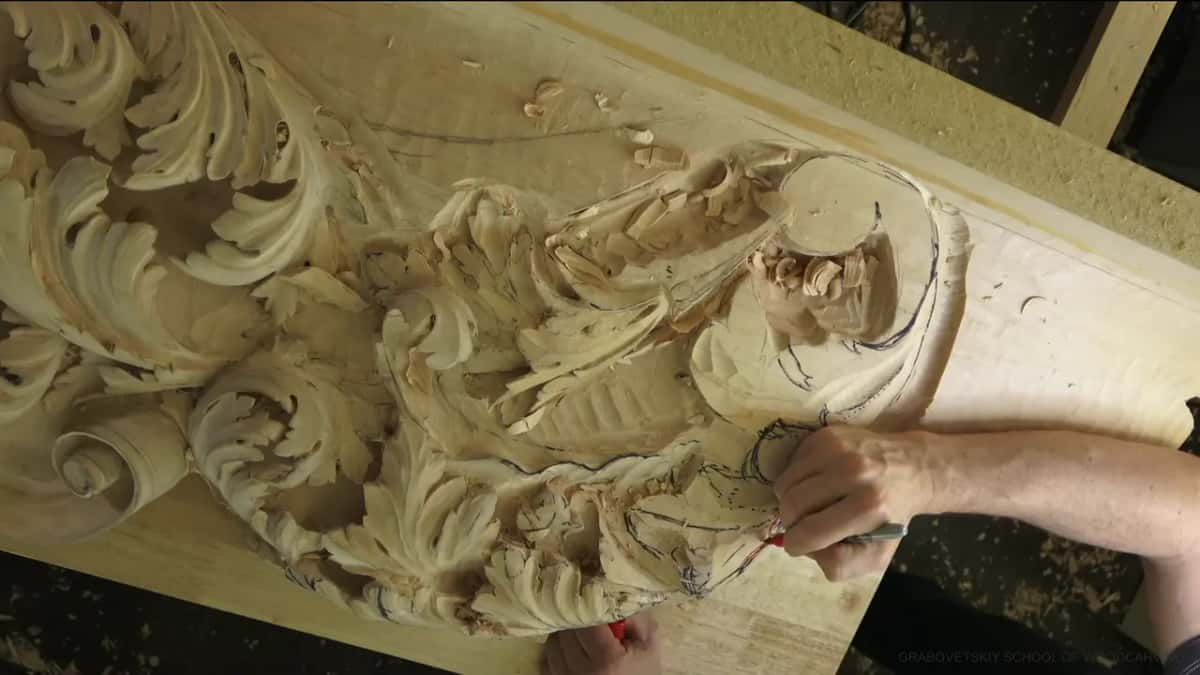 His fingers pinch a red marker and draw a boundary low on the carving, over older black lines.