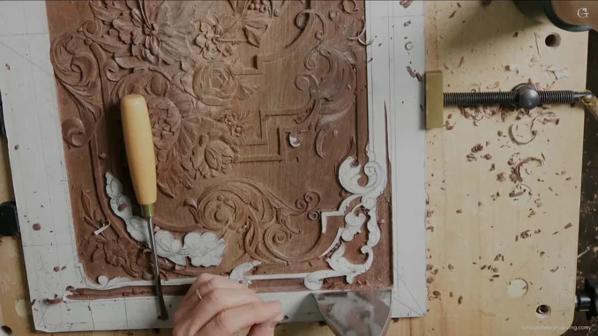 A long chisel stands upright on the lower border while one hand holds a wide blade below it