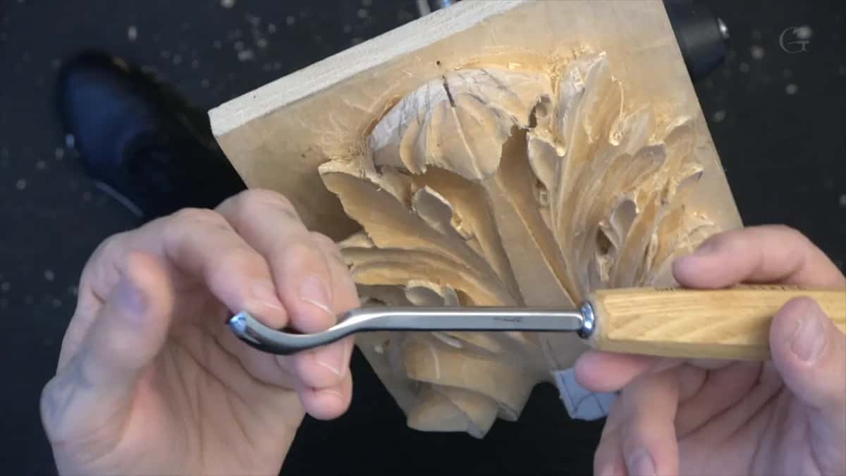 A spoon bent tool held up sideways in both hands, its pale handle off to the right and the panel behind