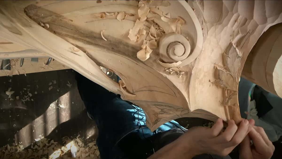 Fingers of both hands pinch a small tool at the lowest tip of the carving