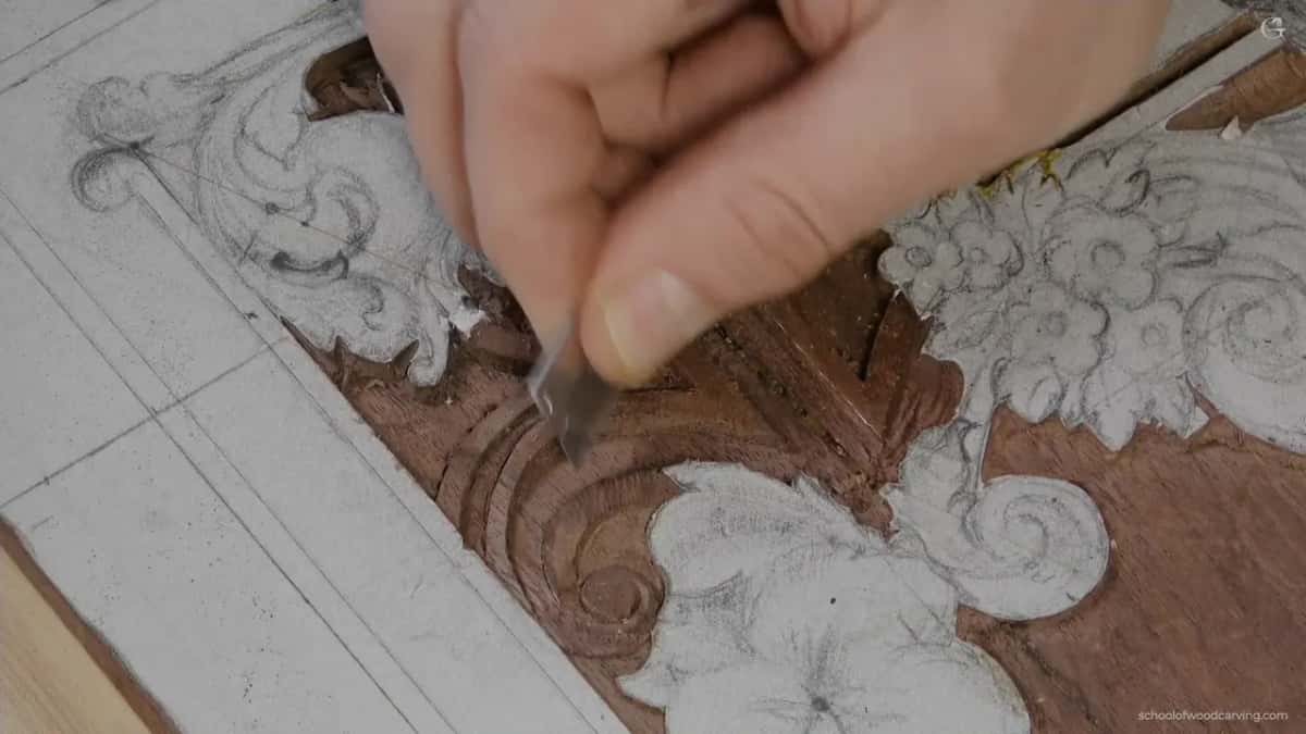 Fingertips press a small flat blade into the stepped corner, flowers to the right