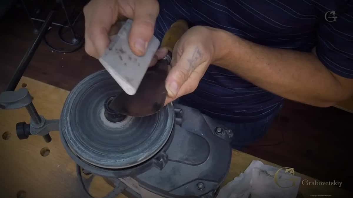 A pale bar pressed against the dark spinning wheel while the other hand holds a gouge
