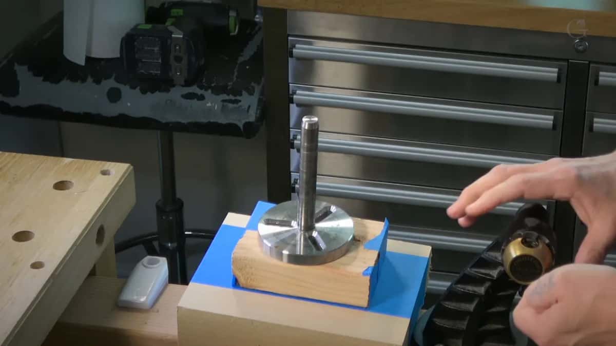 Round steel plate and its post screwed to a block wrapped in blue tape