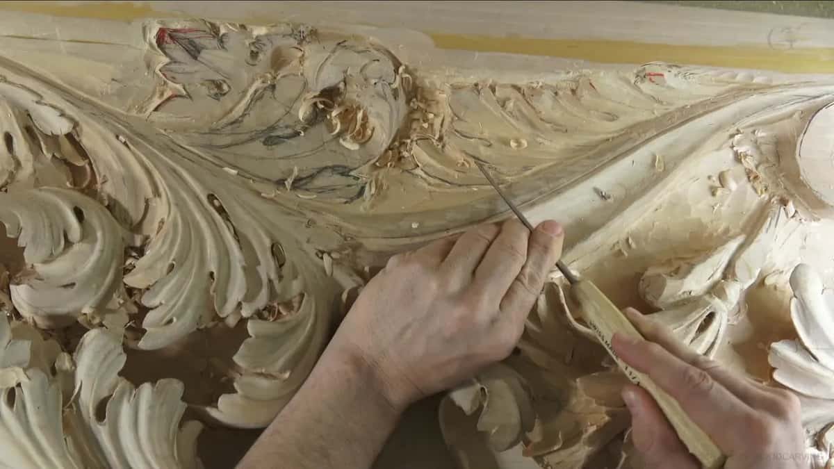 Along a raised ridge below the board's top edge, two hands draw a very small tool.