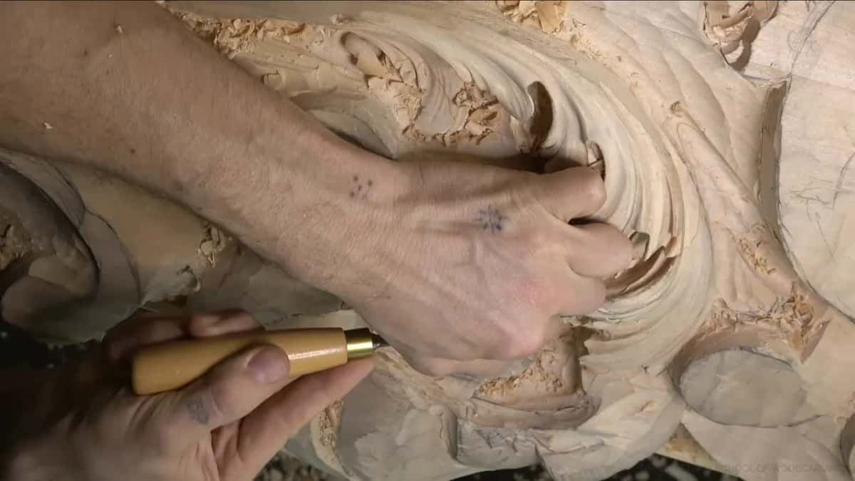 Both hands on the work: one pushes into the lobe, the other holds a pale handle below.