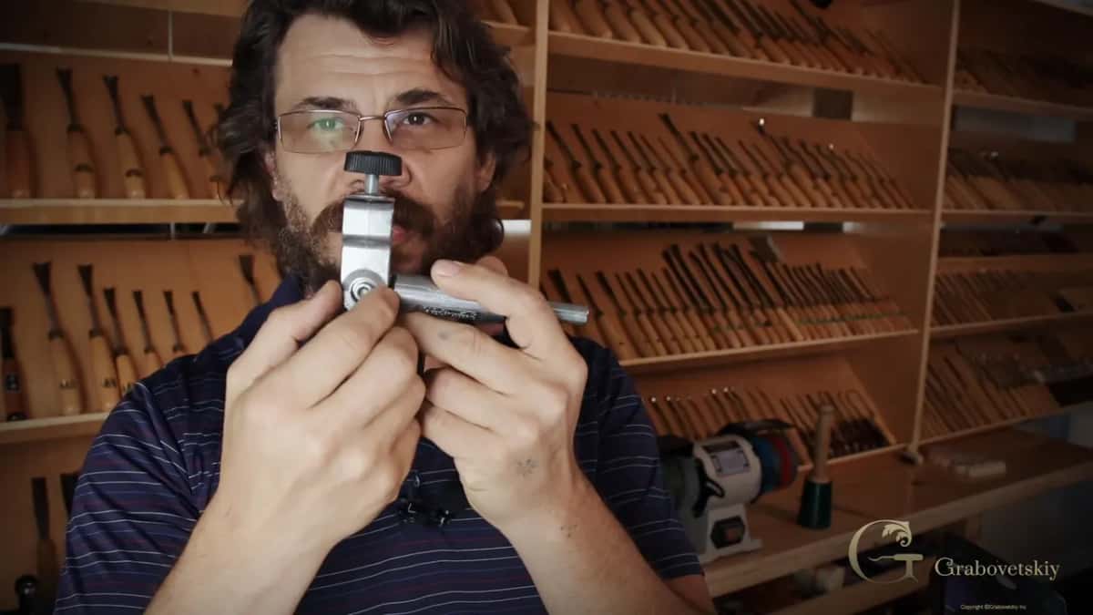 Alexander holds the jig up to the camera in both hands, a black knob on top.