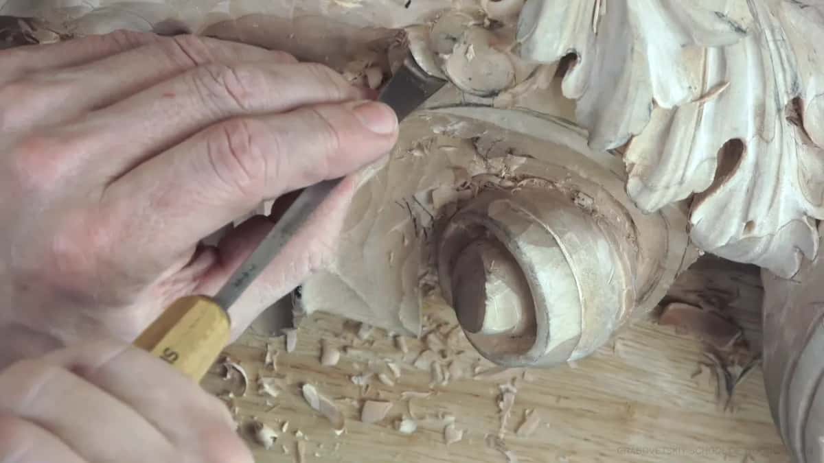 Both hands on a yellow handled gouge, working along the curved edge of the knob.