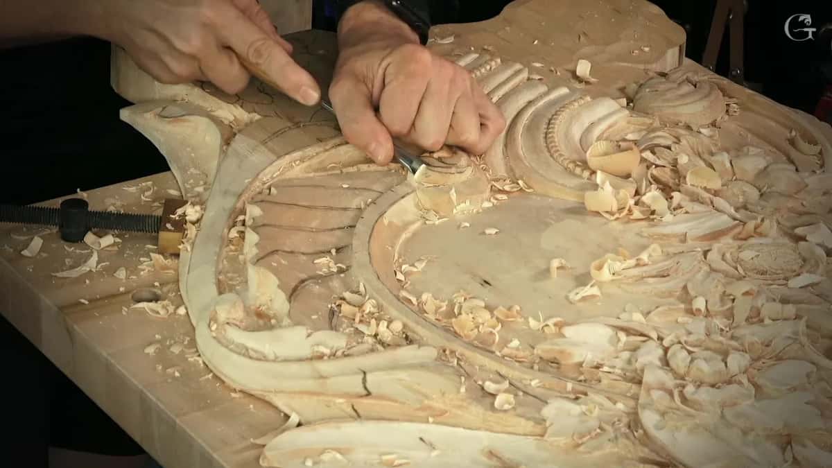 From farther back, one hand steadies the gouge while a finger points along the flutes, and clamps hold the board