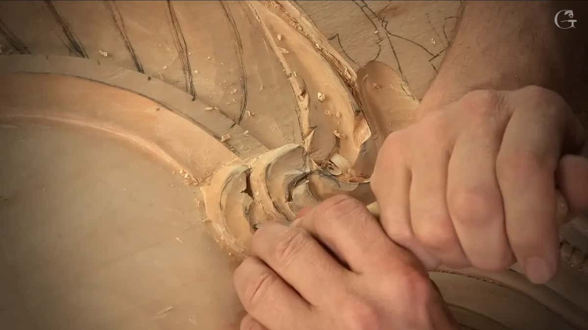 Two hands hold one tool low where the scroll runs into the flutes and the molding next to them