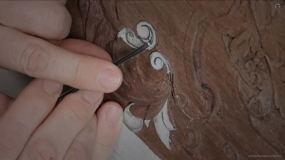 A thin dark blade set along the line of the scroll, with the white paper pattern still on the walnut