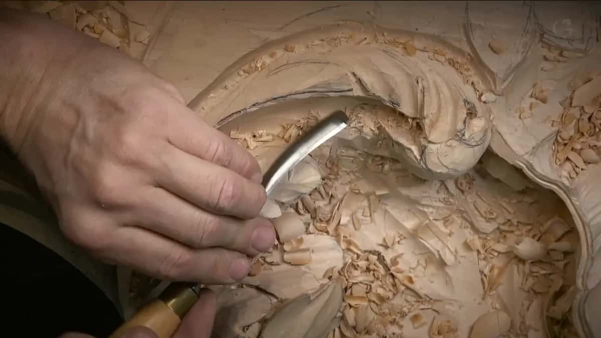 Bent steel dropping into the dark hollow under the finished curl, shavings all round