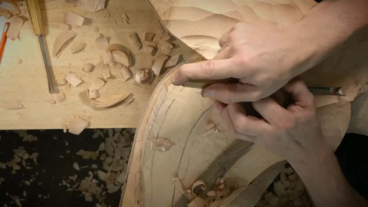 Two hands hold one gouge crosswise and pull it back across the surface toward the carver