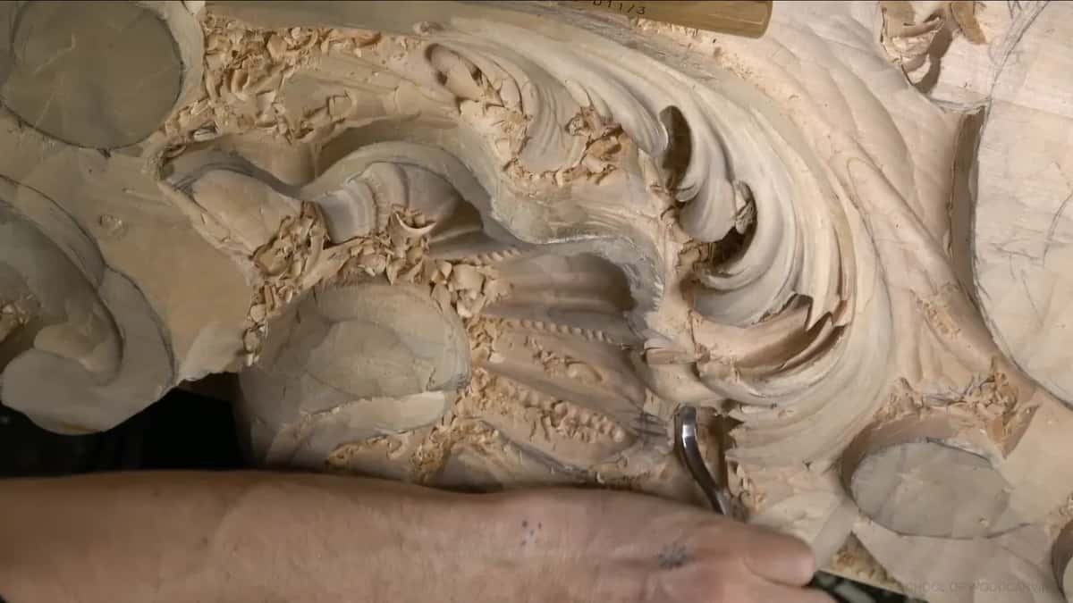 A bent spoon veiner reaching up under the edge of a carved acanthus lobe, one arm across the panel.