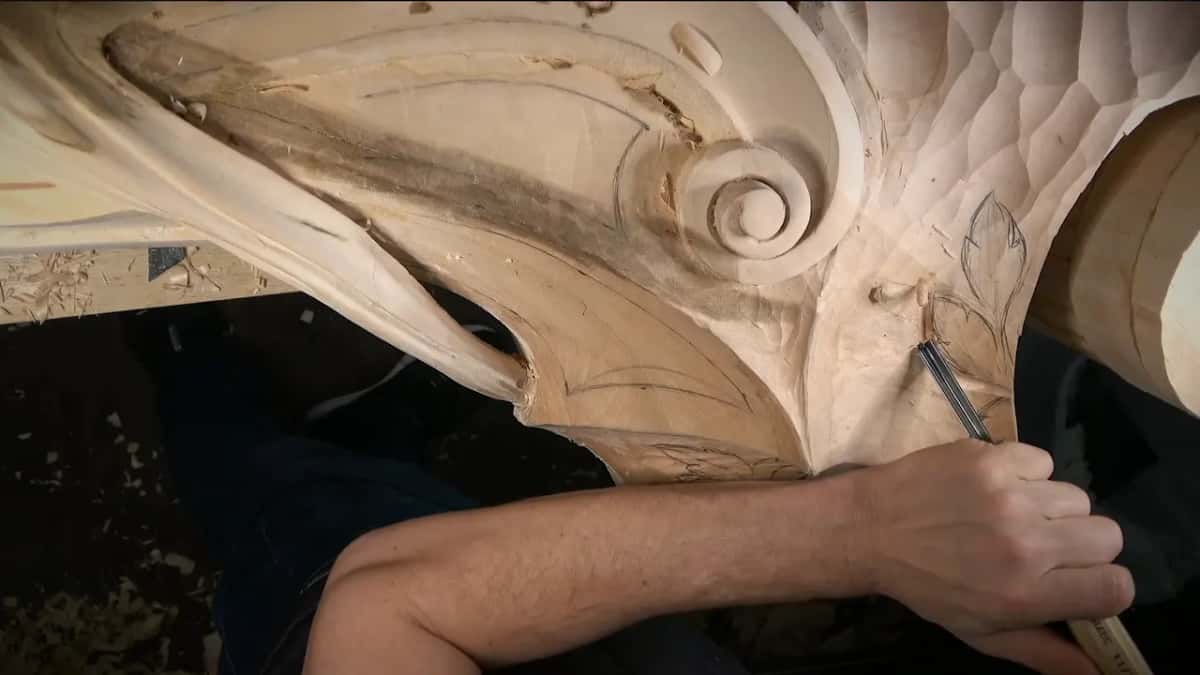 Gouge follows a penciled leaf beside the round scroll, one arm across the block