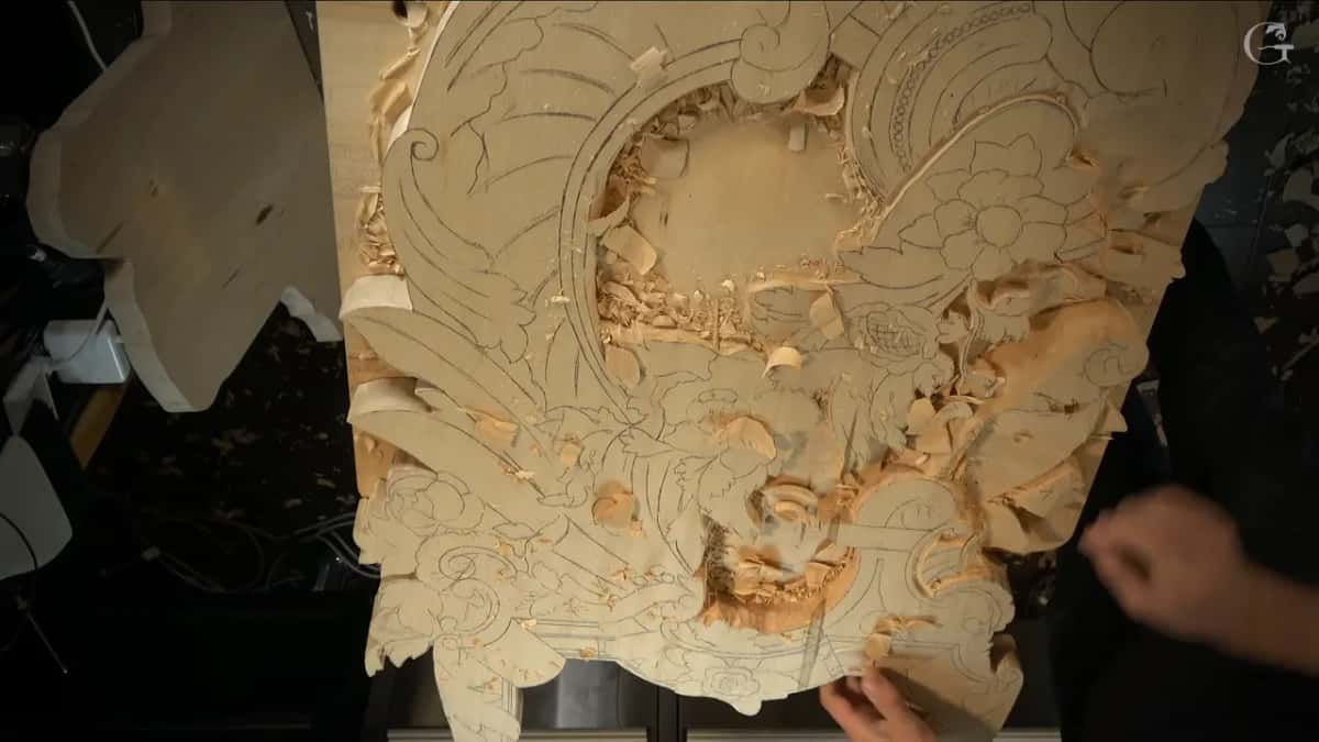 Two hands work the lower right edge of the panel, chips over everything.