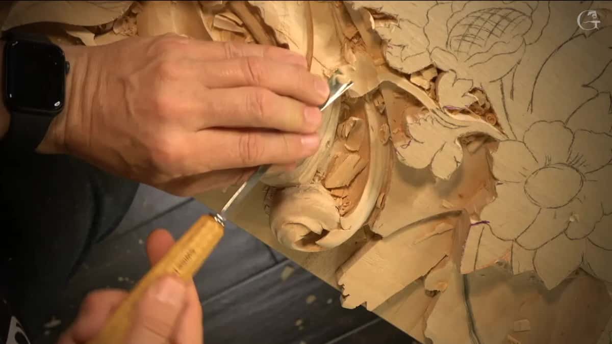 Yellow handle, fingers on the steel, a gouge lowering the wood around the acanthus curl.