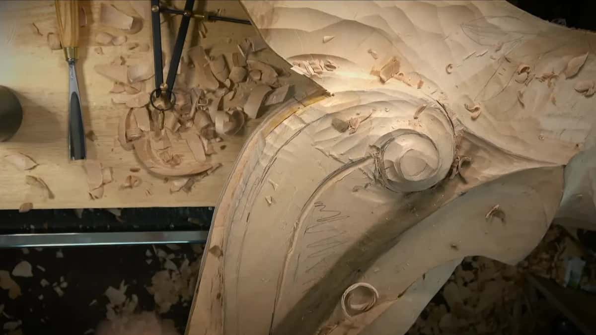 Seen from straight above, a volute scroll with a fresh groove following the inner curve, calipers resting on the bench