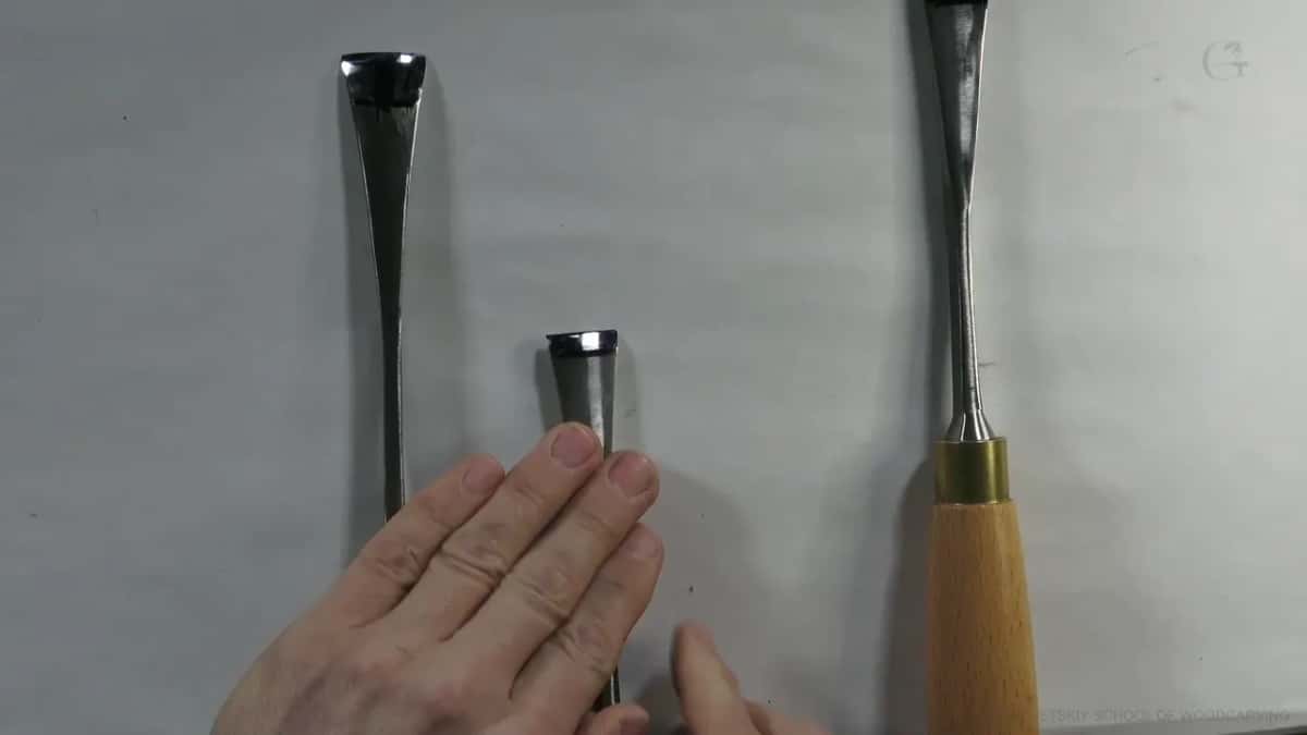 Two fingers press the middle blade flat, a gouge on either side of it