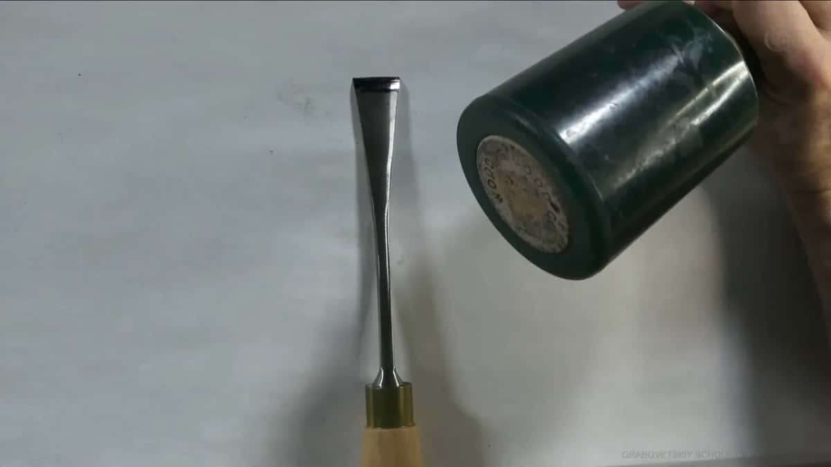 Dark green mallet head held up next to a gouge on white paper