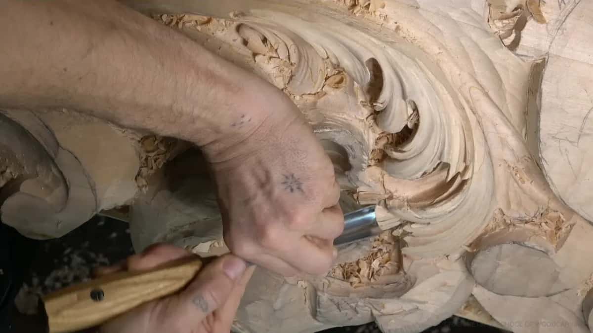 Tattooed hand, wide pale handled gouge.
