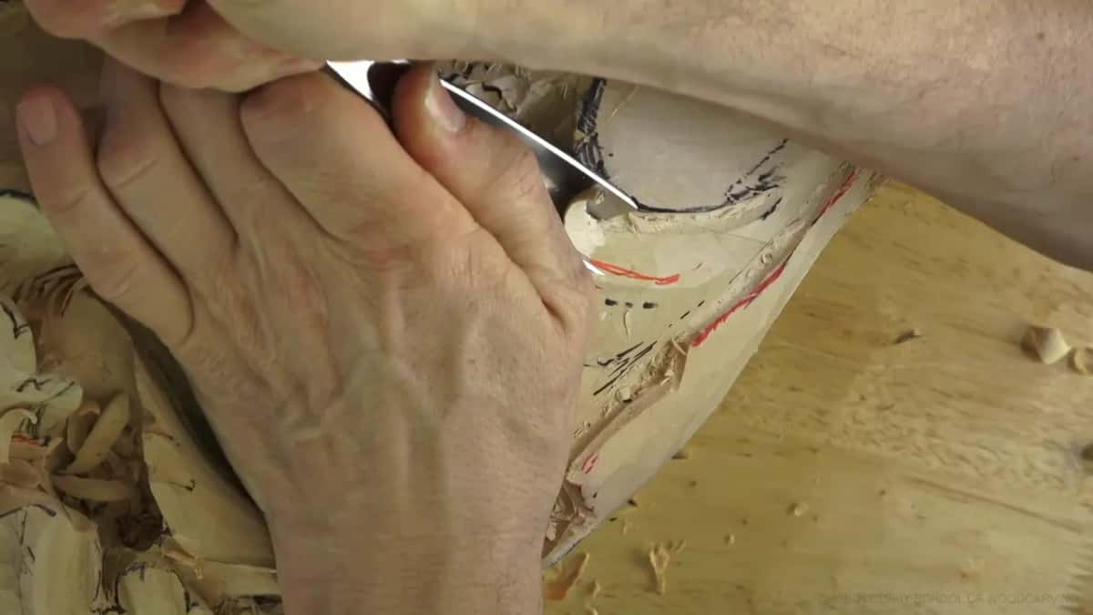 Up close, a wide gouge meets red and black lines on the wood.