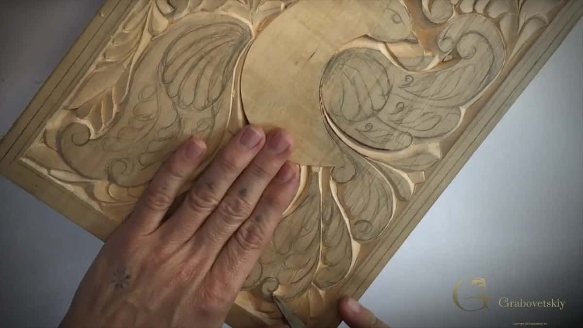 Left hand spread flat across the bird while the knife waits low at the bottom edge of the board