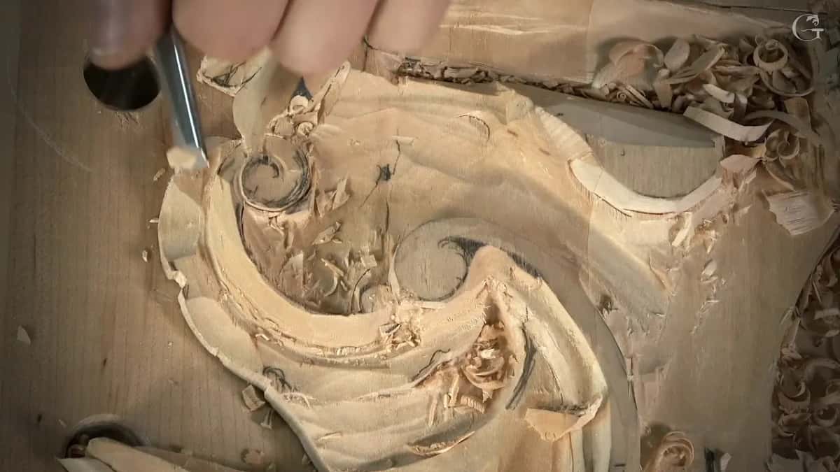 Near a bench dog hole, a narrow gouge works the small curl at the top of the scroll