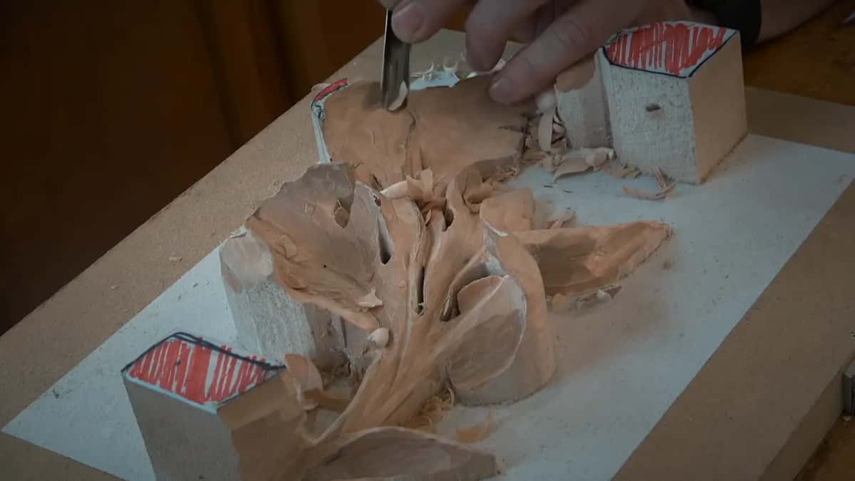 A curved tool rests in the top lobe, fingers pressed on its shank, chips piled behind