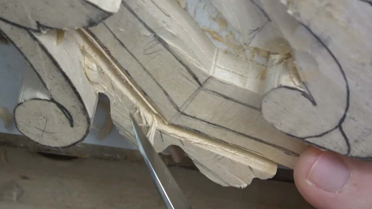 A thumb steadies the piece while a small blade works along the molding below the volute